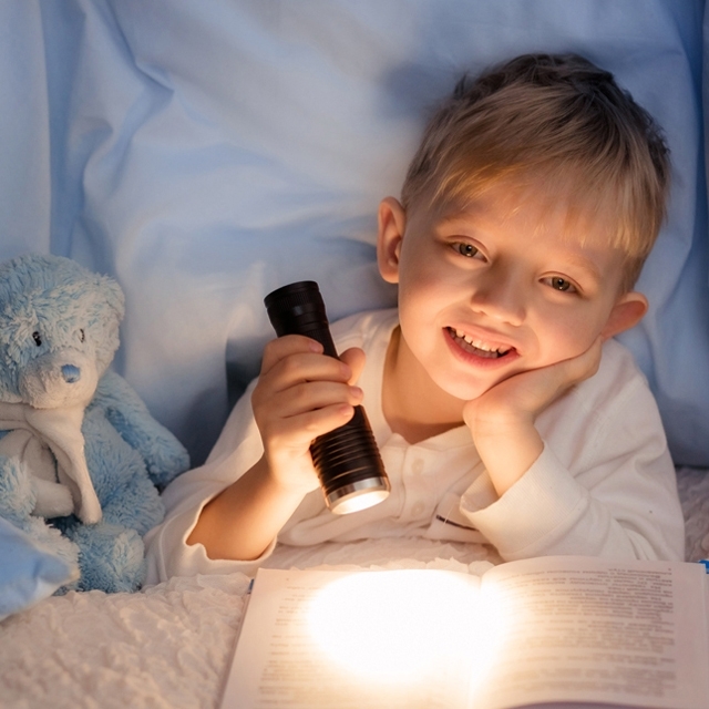 CHAMBRES_ENFANTS_Photographie_640x640_Jeune_garçon_heureux_de_faire_de_la_lecture_dans_son_lit_sous_les_couvertures_éclairé_par_sa_lampe_de_poche