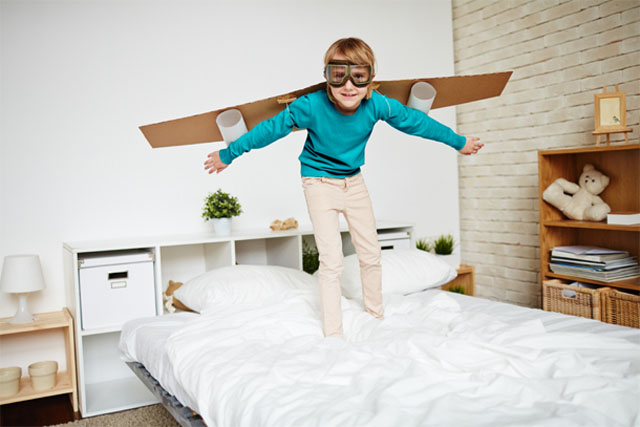 CHAMBRES_ENFANTS_Photo_640X427_Garçon_debout_sur_lit_avec_ailes_avion_dans_le_dos_simulant_un_envol CHAMBRES_ENFANTS_Photo_640X427-Garçon_souriant_debout_sur_son_lit_et_portant_sur_son_dos_des_ailes_en_bricolage_maison_pour_imiter_un_avion_ou_un_super-héros_qui_peut_se_propulser_dans_les_airs